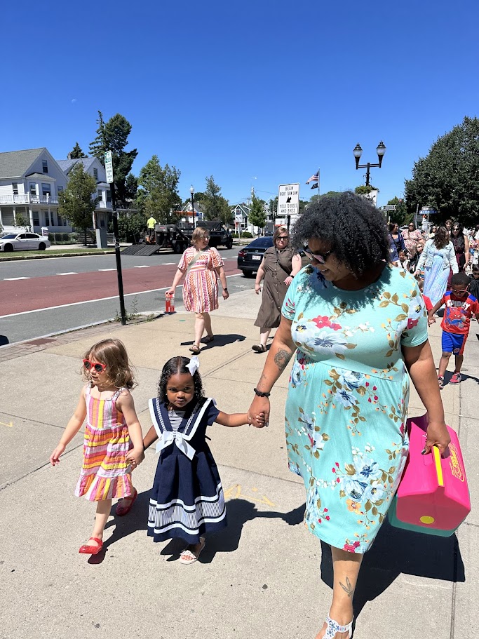 A group of preschool graduates stand in front of the Elizabeth Peabody House with their graduation caps.