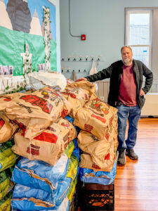 EPH Food Access Program Director Thomas Bouchard standing next to stacked bags with 2050 lbs of potatoes.